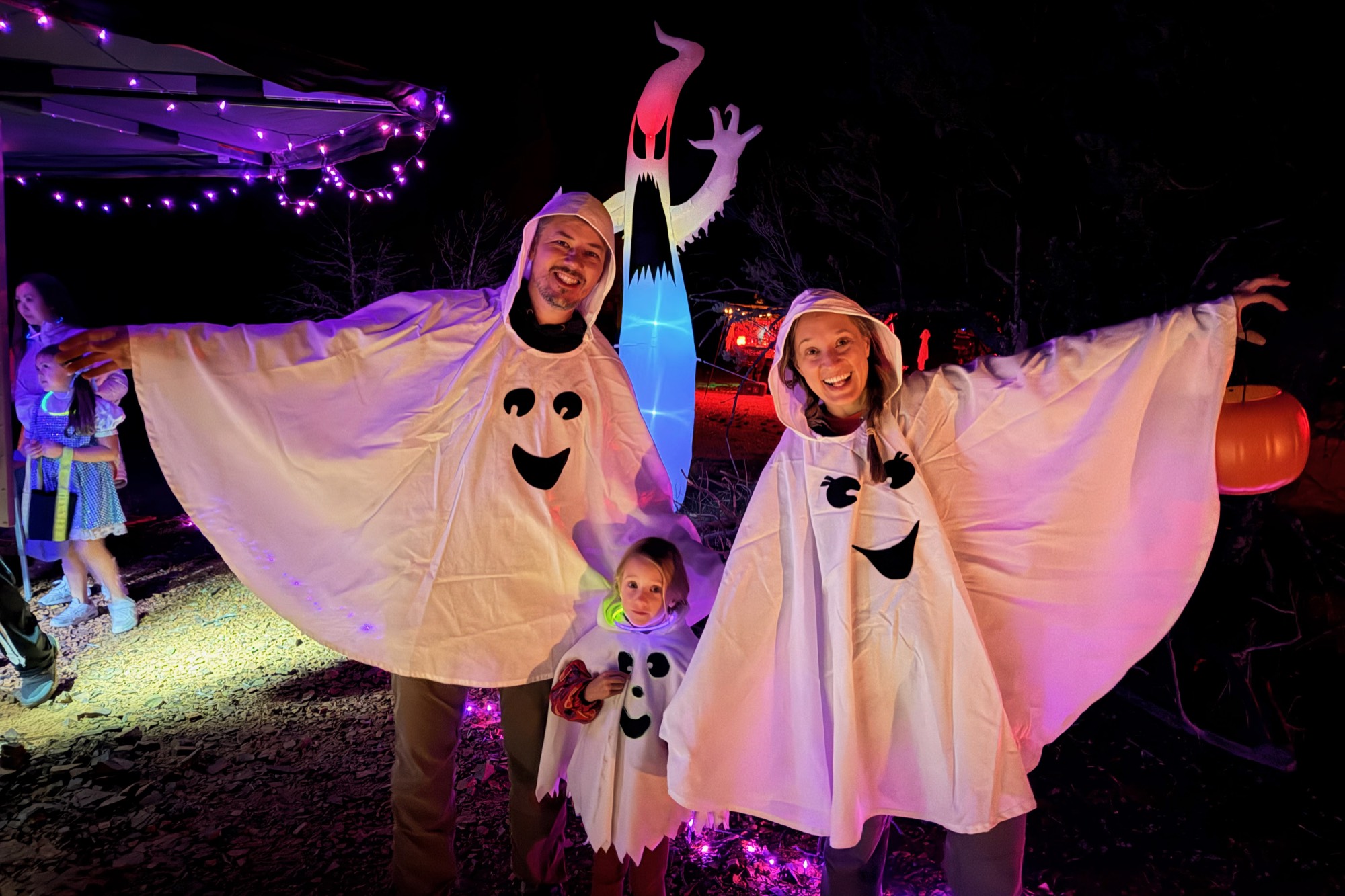 A family dressed as ghosts in front of a camp lit with purple lights